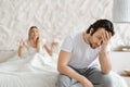 Angry woman shouting at her husband, having conflict while sitting on bed at home, focus on upset man