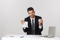 Angry young bearded man work at desk with laptop isolated over white background. Screaming tearing paper documents Royalty Free Stock Photo