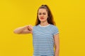 Angry young brunette woman in striped t shirt, looking upset, showing thumb down. Indoor studio shot on yellow background Royalty Free Stock Photo