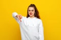 Angry young brunette woman in white casual style sweatshirt, looking upset, showing thumb down. Indoor studio shot on yellow Royalty Free Stock Photo