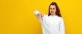 Angry young brunette woman in white casual style sweatshirt, looking upset, showing thumb down. Indoor studio shot on yellow Royalty Free Stock Photo