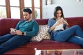 Angry young couple ignoring each other using phone after an argument while sitting on sofa at home Royalty Free Stock Photo