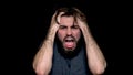 Angry young man shouting, expressing negative emotions, tearing his hair out, isolated on black background. Close up of Royalty Free Stock Photo