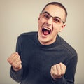 Angry young man shouting with open mouth and very anger face, showing the fists in fashion glasses Royalty Free Stock Photo