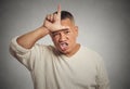 Angry young man showing loser sign on forehead