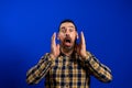 Angry young man yelling screaming. Hipster man with beard in blue plaid checkered shirt Isolated on gray studio Royalty Free Stock Photo