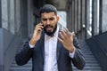 Angry young Muslim businessman talking on the phone near an office building Royalty Free Stock Photo