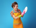 Angry young woman with sponge washing dish on blue