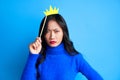 Angry young woman with paper crown on stick on blue background.