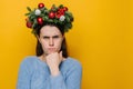 Angry young woman in traditional Christmas wreath looking at camera with gloomy sad expression, feeling insulted or offended