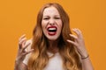 Angry young woman with wavy redhead, screaming on yellow studio background Royalty Free Stock Photo