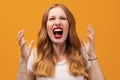 Angry young woman with wavy redhead, screaming on yellow studio background Royalty Free Stock Photo