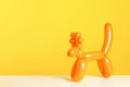 Animal figure made of modelling balloon on table against color background.