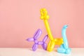 Animal figures made of modelling balloons on table against color background.