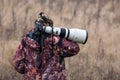 Animal Photographer. Photo Hunter. A Man In Camouflage Uniform With A Black Camera And A Large White Lens. A Man With A Camera On Royalty Free Stock Photo