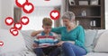 Animation of heart icons over caucasian grandmother and grandson reading book in livin groom