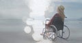 Animation of light spots over disabled cuacasian woman sitting in wheelchair at beach