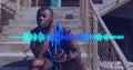 Animation of soundwave over african american man on training break using earphones with smartphone