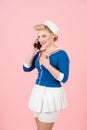 Anime style female talks over smart-phone on rose background. Attractive sailor girl with blonde curl and pin-up makeup