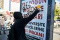 Protester wearing a black hoodie writes a slogan on an advertising sign board on the street with paint spray during Gezi park