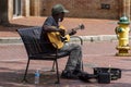 An elderly African American man playing guitar on a street bench