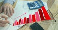 Annotating finance sheets at wooden desk, hands with light blue cuff holding pen and chart overlay Royalty Free Stock Photo
