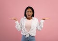 Annoyed African American woman gesturing I DON`T KNOW, shrugging her shoulders on pink studio background Royalty Free Stock Photo