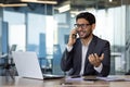 Annoyed and angry hispanic businessman talking on phone, man at workplace inside office with laptop Royalty Free Stock Photo