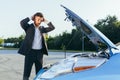 An annoyed and angry man, near a broken car, tries to call an insurance agent and a repair crew. for car repair Royalty Free Stock Photo