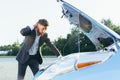 An annoyed and angry man, near a broken car, tries to call an insurance agent and a repair crew. for car repair Royalty Free Stock Photo