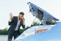 An annoyed and angry man, near a broken car, tries to call an insurance agent and a repair crew. for car repair Royalty Free Stock Photo