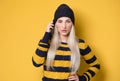 Annoyed beautiful girl on the phone, model wearing woolen cap and sweater, isolated on yellow background. Annoying woman talking