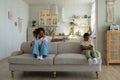 Annoyed Black mother sitting with offended son on sofa talking on phone. Parents and discipline