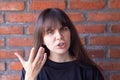 Annoyed brunette woman with bangs wearing a black t-shirt screaming due to conflict, showing all anger and anger on brick wall Royalty Free Stock Photo