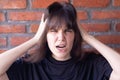 Annoyed brunette woman with bangs wearing a black t-shirt screaming due to conflict, showing all anger and anger on brick wall Royalty Free Stock Photo