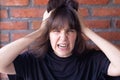 Annoyed brunette woman with bangs wearing a black t-shirt screaming due to conflict, showing all anger and anger on brick wall Royalty Free Stock Photo