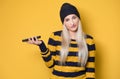 Annoyed girl on the phone, model wearing woolen cap and sweater, isolated on yellow background. Annoying young woman using mobile