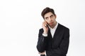 Annoyed guy talking on phone and roll eyes, tired of boring conversation, boring person on call, standing in black suit Royalty Free Stock Photo