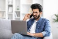Annoyed indian man using phone while looking at his laptop at home Royalty Free Stock Photo