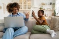 Annoyed mother working on laptop asking child not to disturb her