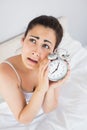 Annoyed woman holding an alarm clock in bed