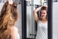 Annoyed young girl holding her damaged long hair in mirror