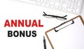 ANNUAL BONUS text written on the white background with keyboard, paper sheet and pen