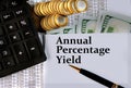 ANNUAL PERCENTAGE YIELD - words on a white sheet on the background of a calculator, coins and dollar bills