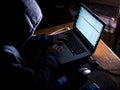 Anonimous man in the hoodie in dark studio typing text online on internet with copy space