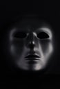 Anonymous black mask protruding from pitch black background. Royalty Free Stock Photo