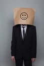 Anonymous businessman hiding his head behind happy smile emoticon on gray background Royalty Free Stock Photo