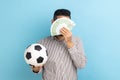 Anonymous businessman holding soccer ball and covering face with fan of euro bills, sports betting.