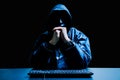 Anonymous computer hacker in white mask and hoodie. Obscured dark face with keyboard computer in the dark. Data thief, Royalty Free Stock Photo