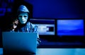 Anonymous computer hacker in white mask and hoodie.Obscured dark face using laptop computer for cyber attack and calling Royalty Free Stock Photo